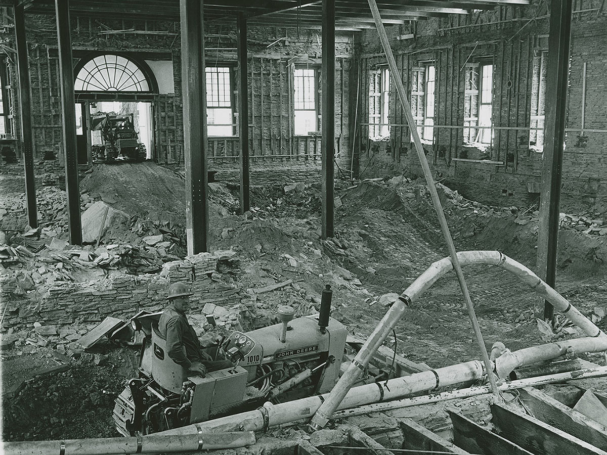 A construction worker drives a bulldozer inside the gutted interior of Alumni Hall