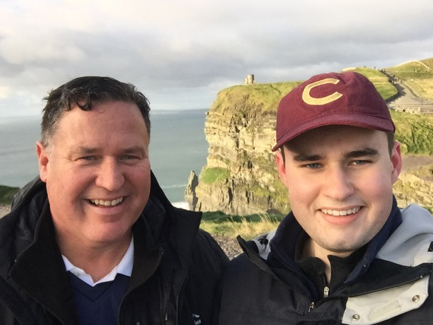 Father and son, wearing C hat, atop Cliffs of Moher