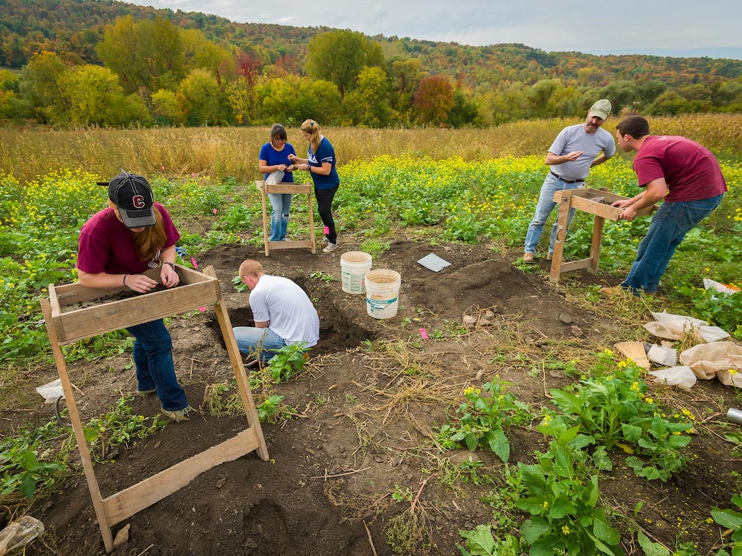 Students digging for artifacts while consulting their professor